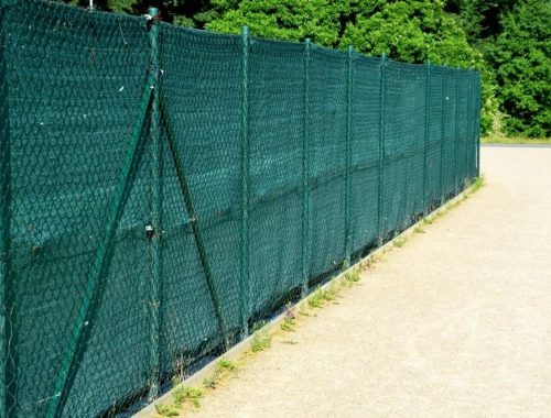 A chain-link fence enhanced with green fabric demonstrates a professional shade cloth installation, providing privacy and sun protection for outdoor spaces