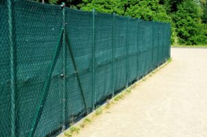 A chain-link fence enhanced with green fabric demonstrates a professional shade cloth installation, providing privacy and sun protection for outdoor spaces