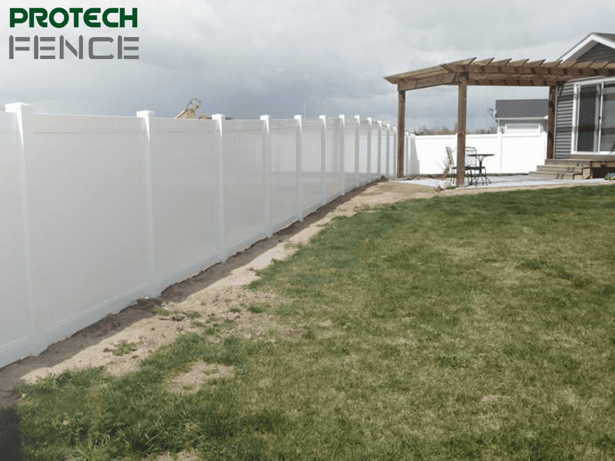 A white vinyl privacy fence runs along the backyard of a suburban home with a pergola, illustrating the potential cost considerations when asking how much does a privacy fence cost per foot.
