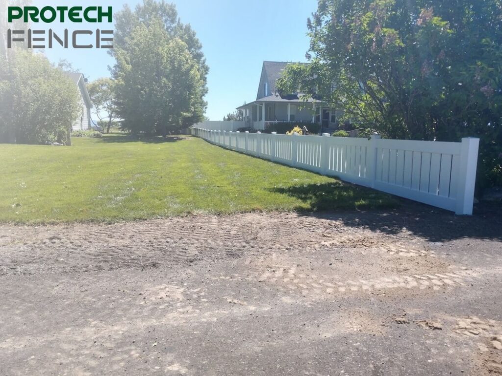A vinyl fence installation pocatello installed along a lush green lawn with Protech Fence logo at the top left corner, showcasing the smooth white panels and clean lines providing privacy and enhancing the property's curb appeal.