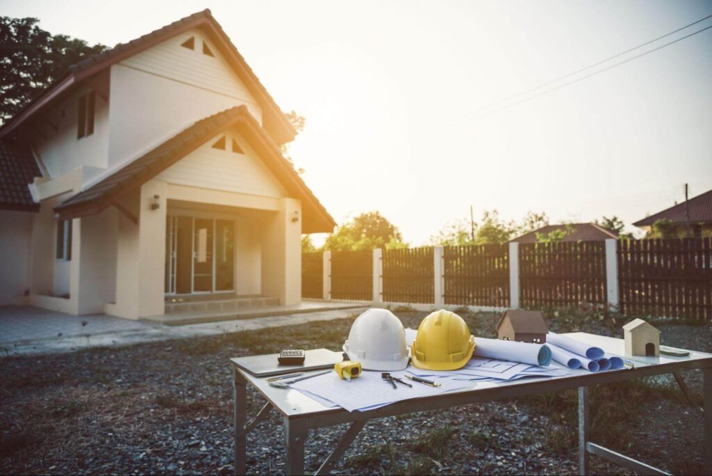 A table with construction plans and hard hats outside a house, illustrating aluminum fence cost per linear foot.