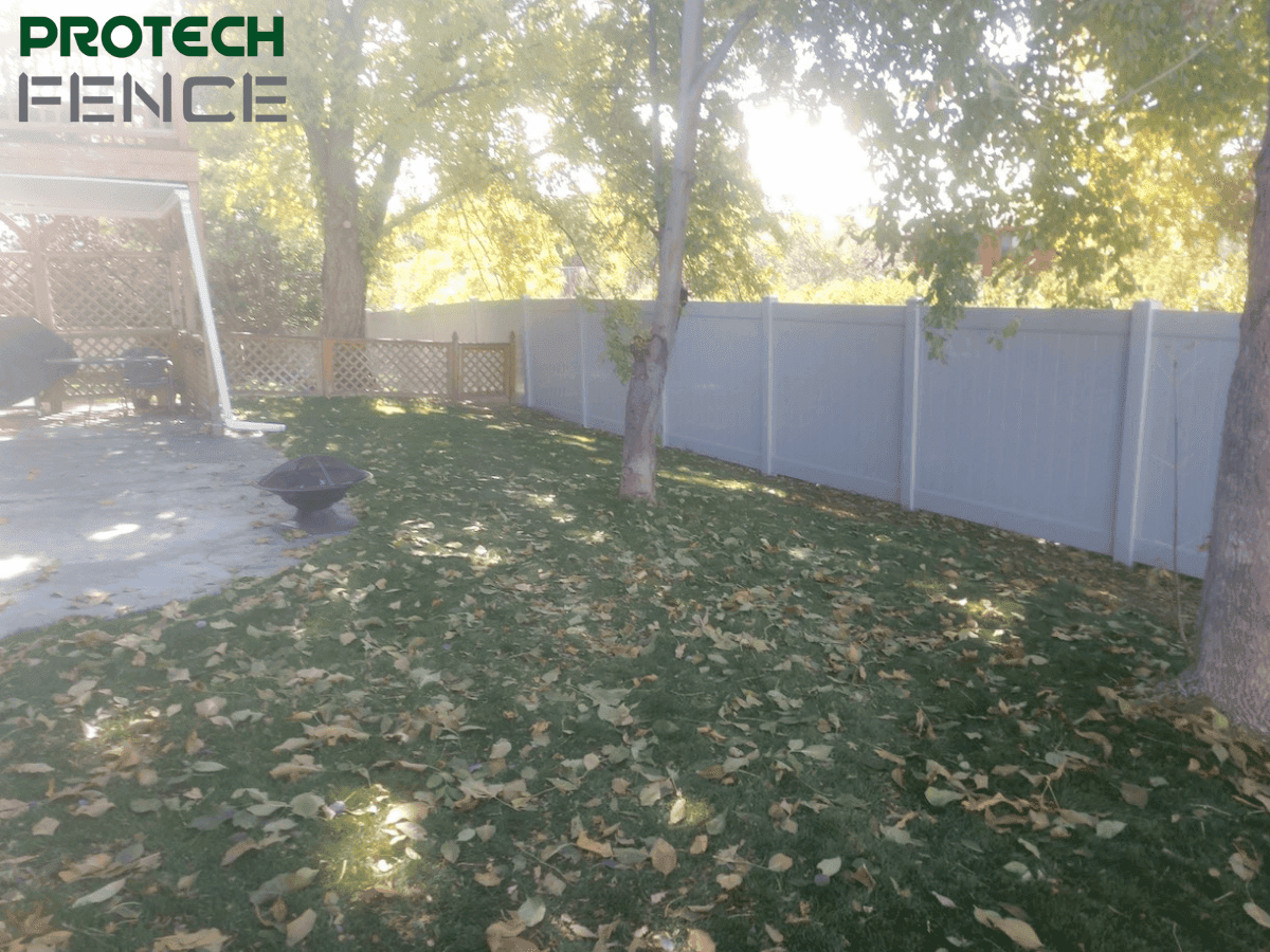 A white privacy fence stands tall in a backyard bordered by trees, highlighting considerations for homeowners wondering how much does a privacy fence cost per foot.
