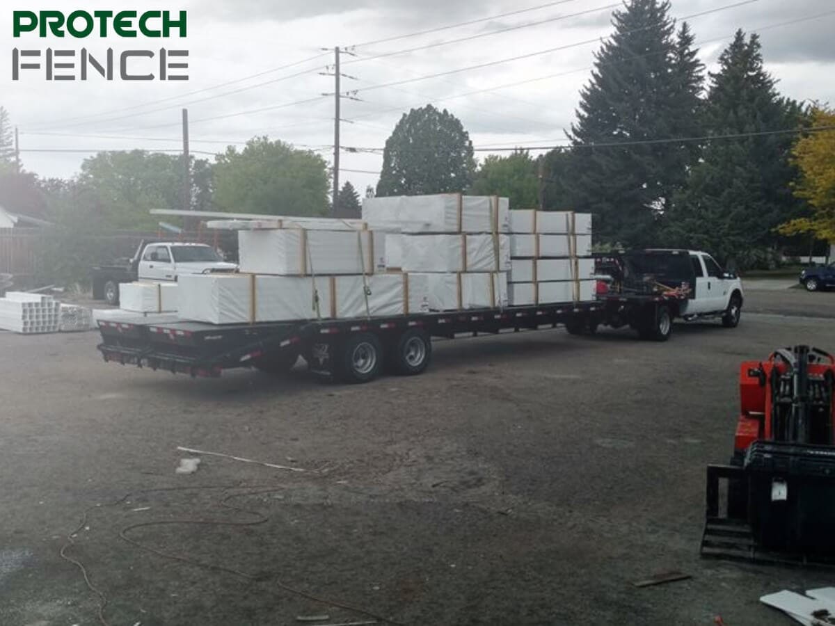 A Protech Fence company flatbed trailer loaded with neatly stacked fence supplies, ready for fence repair Pocatello projects, parked in a gravel lot with trees in the background. 