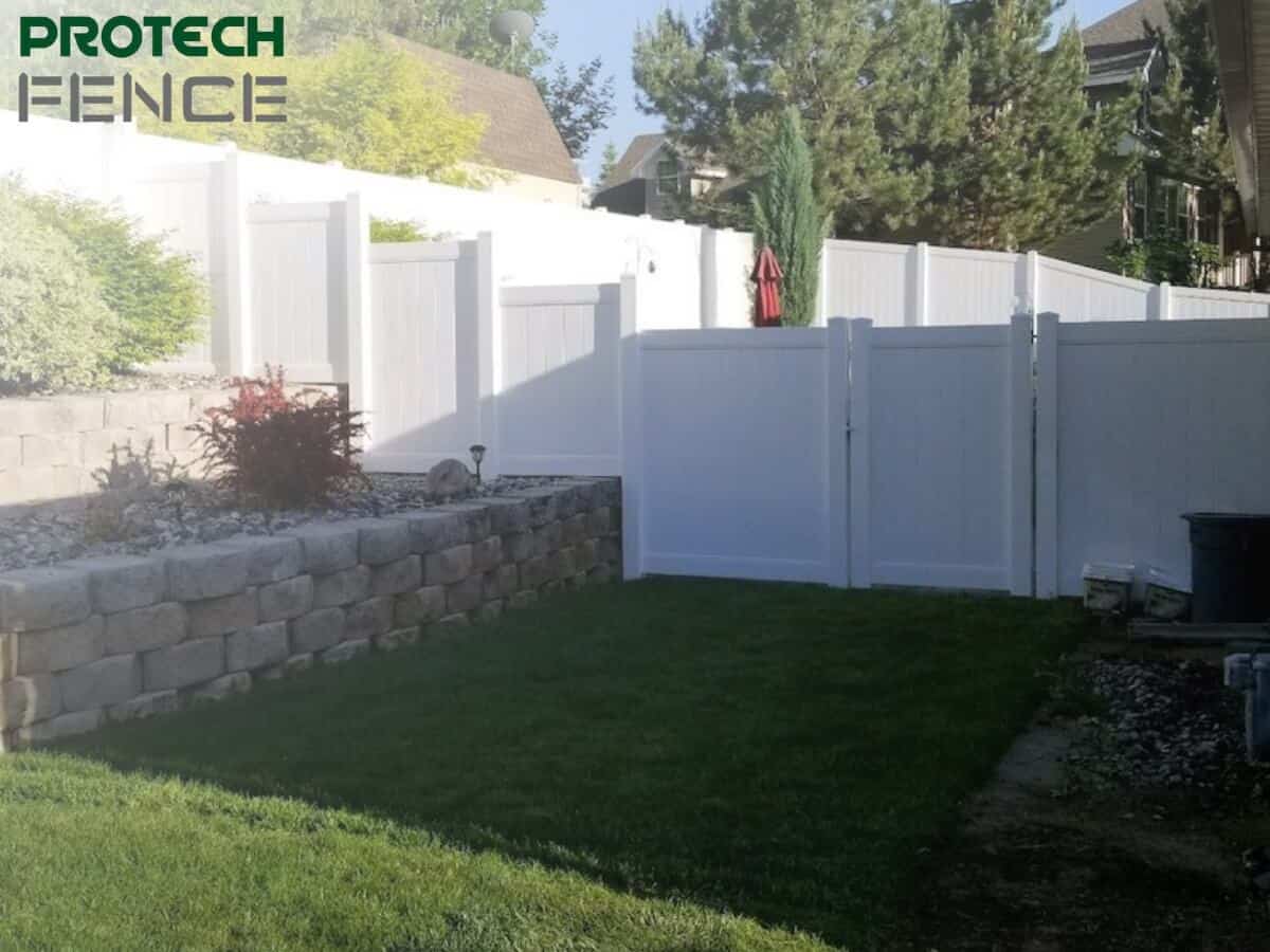  A continuous stretch of white vinyl fencing extending along the boundary of a residential lawn, epitomizing the use of a white vinyl fence for privacy fence needs. The image shows the fence's solid panels and post caps, providing a secure and private outdoor area while offering a modern, clean appearance to the property. 