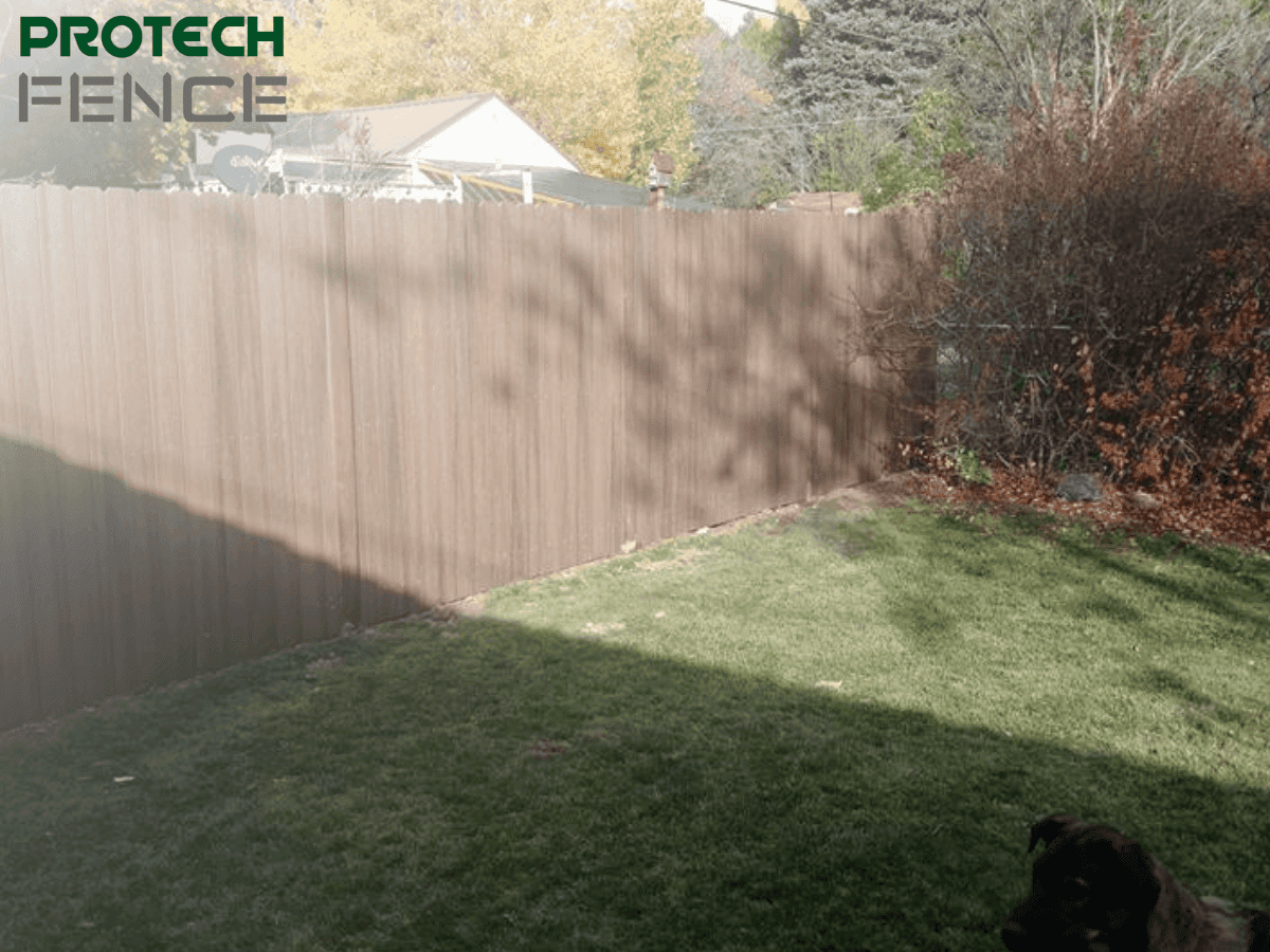  A backyard with a well-maintained lawn is enclosed by a tall, dark-stained wooden fence. In the foreground, a dog is partially visible. The image showcases a typical residential fence, relevant for understanding how much it costs to build a wooden fence.
