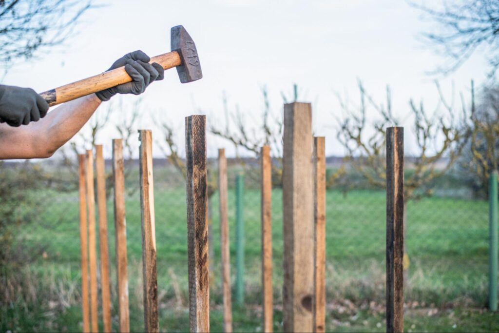 A person installing a wood fence, demonstrating how much does a wood fence cost per foot in a backyard setting.