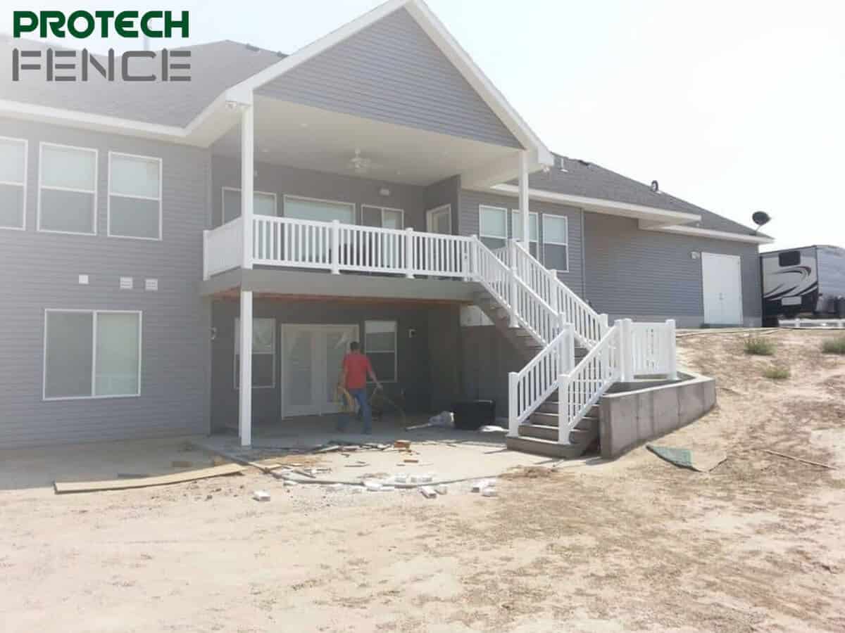 Deck contractors Pocatello working on a new deck installation at a residential home with a two-story gray siding exterior, featuring white railing and stairway, with the Protech Fence logo at the top