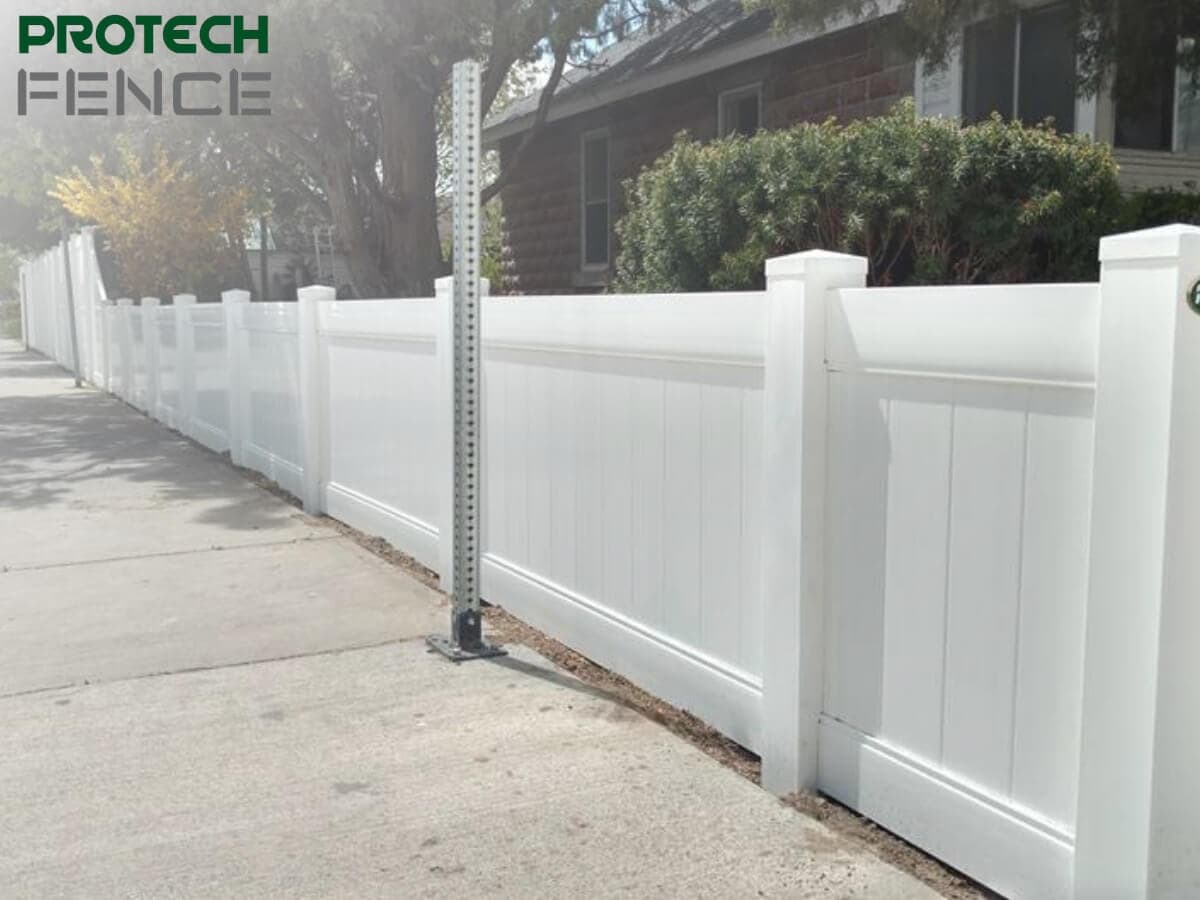 A vinyl fence installation pocatello with vertical paneling and caps running along a sidewalk, featuring the Protech Fence logo in the top left, illustrating the fence's clean appearance and sturdy posts against an urban backdrop.
