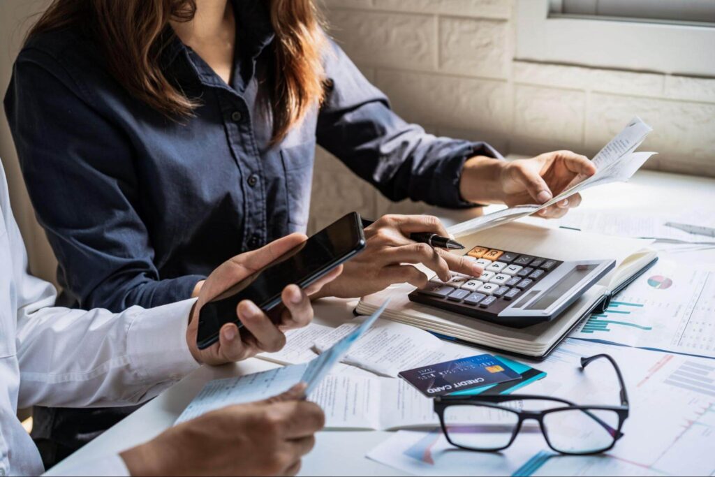 Two people calculating expenses with documents, a calculator, and a credit card, illustrating the question: how much does a privacy fence cost per foot.