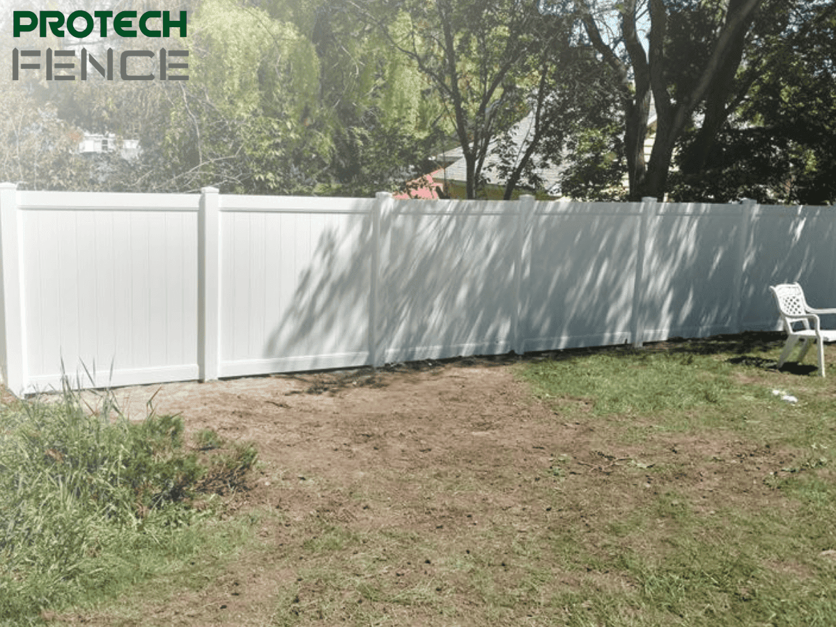 A white privacy fence encloses a backyard with leafy trees and a patio area, providing a visual reference for homeowners considering how much does a privacy fence cost per foot.
